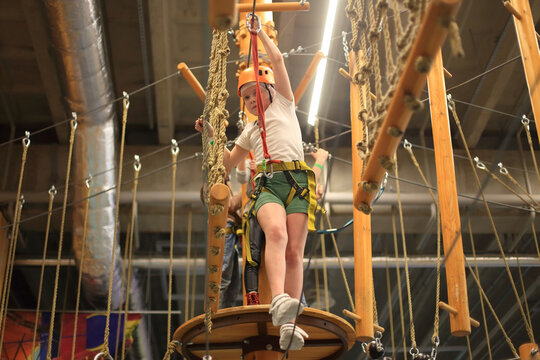 a child navigating a challenging rope course at a children's activity center. Dressed in protective gear, the young adventurer traverse the intricate pathways suspended high above the ground - Powered by Adobe