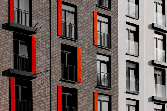 Modern apartment facade with brick walls, black-framed windows, and striking vertical red and orange