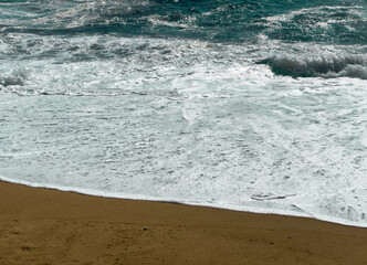 Waves roll onto a sandy shore with white foam spreading across the beach, creating a dynamic and