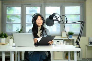 Young woman podcaster wearing headphones recording audio with microphone at home studio