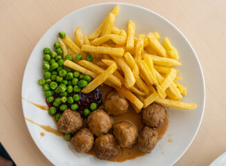Meatballs with french fries, green peas, bechamel sauce and cranberry jam