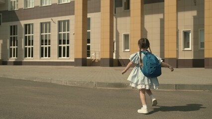 elementary school child is running around the school yard with backpack on his shoulders, small kid...