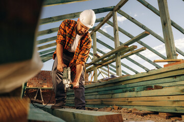 Drilling the holes in plank. Construction worker is on the roof of a house