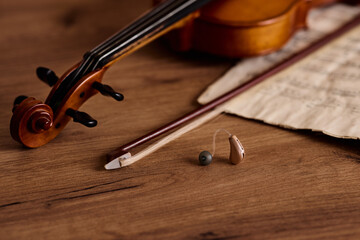 BTE hearing aid next to a violin and bow on wood, highlighting auditory solutions for music lovers