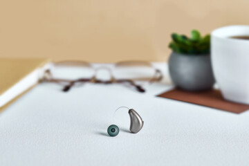 BTE hearing aid sits on a desk beside glasses and a plant, showcasing modern health solutions