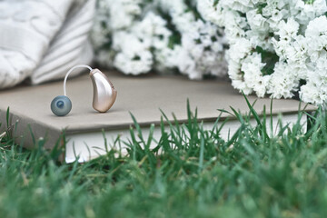 Hearing aid rests on a book amidst greenery and white flowers, creating a peaceful scene. Hearing...