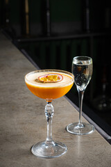A vibrant orange cocktail with a fruit slice sits next to a sparkling drink on the counter