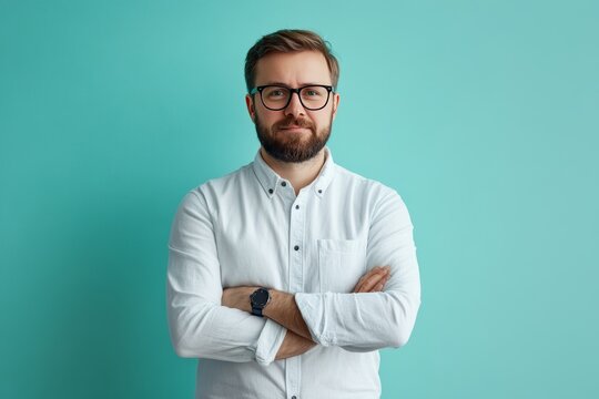 Man with glasses and a beard stands confidently with arms crossed against a teal background.
