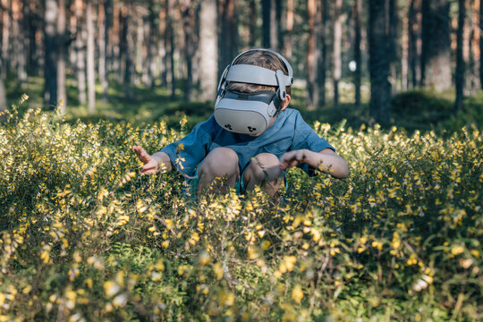 Child in virtual glasses looks at flowers in forest