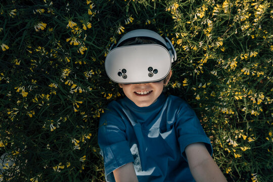Child in virtual glasses lies in flowers and smiles