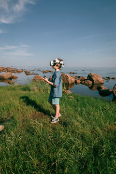 Child in virtual glasses in grass on seashore