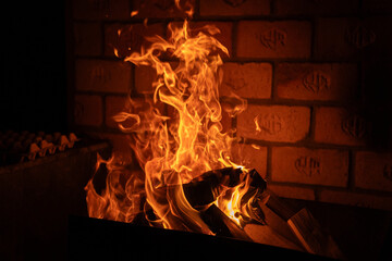 Close-up view of bright orange flames rising from burning firewood inside a brick fireplace,...