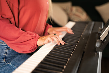 Obraz premium Close-up of woman's hands playing on an electronic piano home in daylight, distance learning of digital classical piano indoors, selective focus