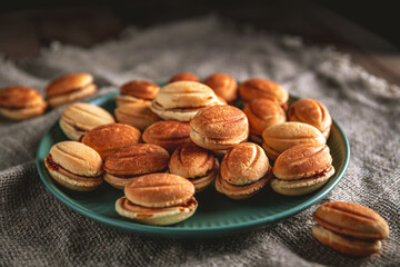 Nut shaped cookies filled with boiled condensed milk are arranged on a teal plate, creating a visually appealing and tempting display of sweet treats
