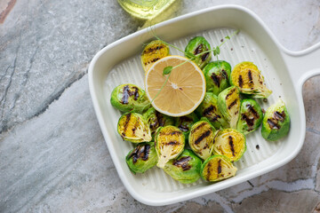Roasted Brussels sprouts in a beige serving tray, horizontal shot on a grey granite background, high angle view