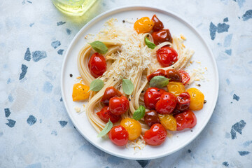 Linguine with roasted cherry tomatoes and grated cheese, horizontal shot on a white and blue granite background, elevated view