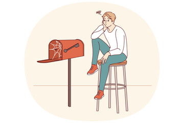 Lonely man waiting for letter, sitting by empty mailbox covered with cobwebs, wanting to receive messages from girlfriend. Lonely guy needs communication and suffers due to lack of friends