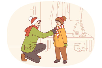 Caring father helps kid put on winter clothes so as not to freeze while walking along cold street. Happy father tying scarf to child showing care and desire to help smiling pre-teen son