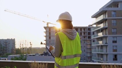 Construction female engineer taking notes and writing on clipboard while inspecting a building site