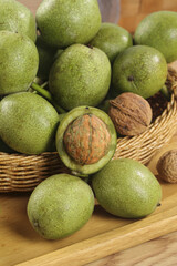 Fresh Green Walnuts in Husks with Shelled Nuts in Wicker Basket on Wood Table