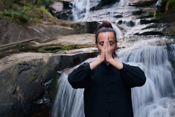 Woman practicing Tai Chi in nature, wearing a traditional black martial arts uniform, standing...