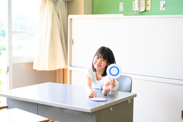 クイズに答える女子学生　学校の教室で○✕を出す教育イメージ