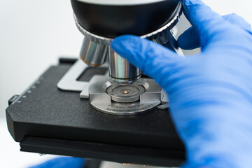 Gloved hands adjusting a microscope with precision in a laboratory setting, engaging in scientific research and analysis to uncover new findings in biology and healthcare