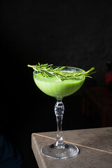 A vibrant green cocktail sits elegantly in a crystal glass, topped with fresh herbs, inviting taste