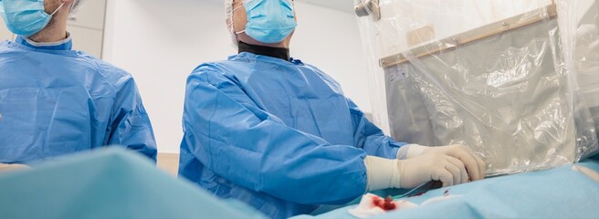 In a bright operating room, two Surgeons wearing blue scrubs and masks perform a delicate heart surgery, displaying focus and expertise. A sterile drape and surgical equipment are visible