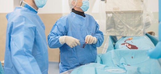 In a brightly lit operating room, two masked medical professionals in gowns and gloves perform a...