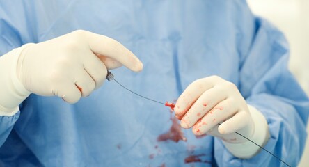 A gloved surgeon in a light blue gown carefully manipulates a medical instrument, possibly a catheter, tinged with blood, in preparation for a procedure inside General Hospital