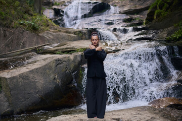 Woman practicing Tai Chi in nature, wearing a traditional black martial arts uniform, standing...