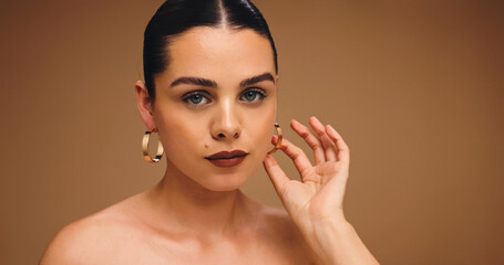 Earrings, beauty and woman with makeup for aesthetic, glow and shine on brown background. Ear...