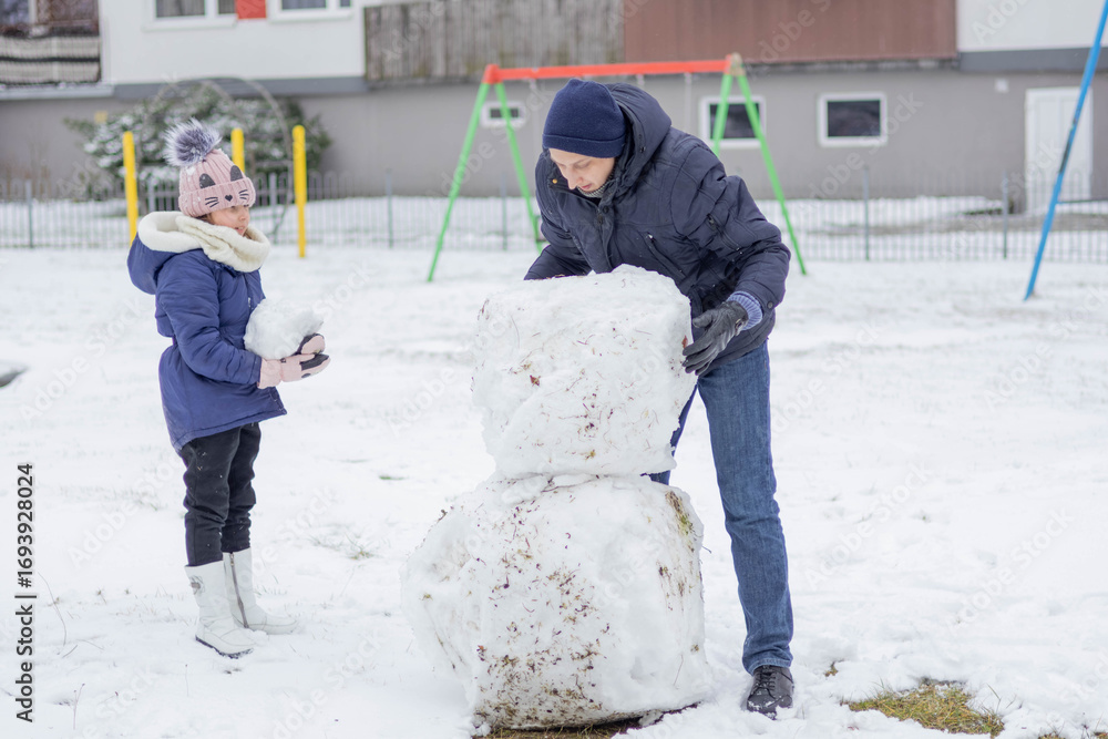 Poster Building a snowman with a child in a winter playground setting