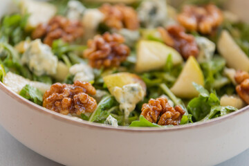 fresh fall salad in a bowl with arugula, ripe pear slices and crunchy walnuts, healthy autumn lunch idea with vibrant colors