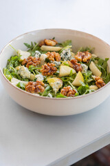 fresh fall salad in a bowl with arugula, ripe pear slices and crunchy walnuts, healthy autumn lunch idea with vibrant colors