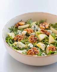 fresh fall salad in a bowl with arugula, ripe pear slices and crunchy walnuts, healthy autumn lunch idea with vibrant colors