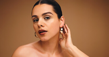 Earrings, beauty and woman with makeup in studio for aesthetic, glow and shine on brown background....