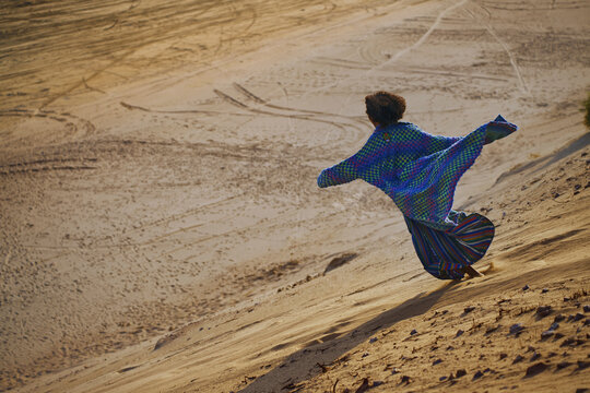 Person in colorful caftan running energetically down sandy desert dune