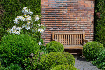 Wooden garden bench with white flowers and brick wall