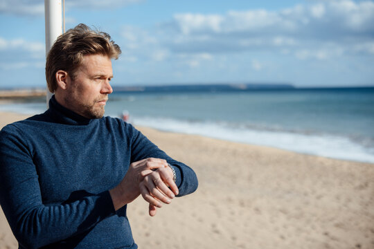 Thoughtful man checking time and looking at sea on beach
