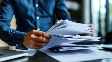 A man in a blue shirt is sorting through a stack of papers on a desk.