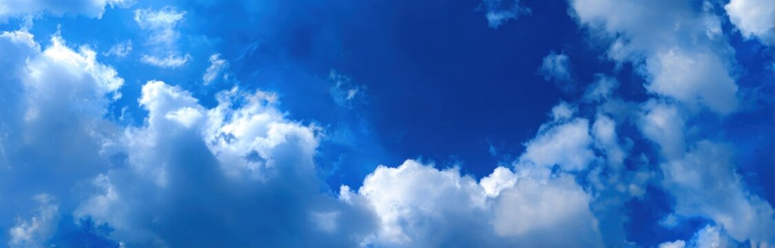 Wide shot of puffy clouds scattered in a vibrant, deep blue sky, creating a sense of openness and serene beauty