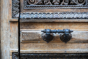 Close-up of ornate carved oak wooden doors with a vintage forged iron handle. The handle features...