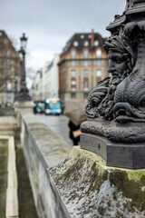 Naklejka premium Close-up of an ornate, historic lamppost on the Pont Neuf bridge in Paris, France. The cast iron base features grotesque mascarons and sea creatures.