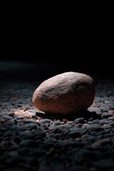 Solitary rock on pebbled ground under dramatic lighting