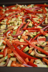 bunch of colorful fall vegetables&mdash;zucchini, red pepper, and carrots&mdash;arranged in a baking tray, drizzled with olive oil and herbs, ready to be roasted
