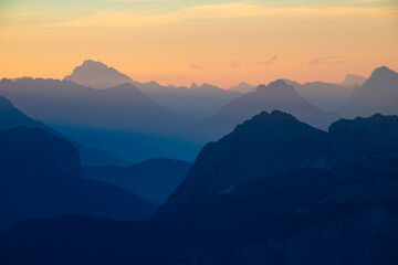 Fototapeta premium Distant mountain peaks layers at sunrise. Pattern of mountains silhouettes against orange sky in Dolomites.