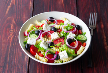 Greek pasta salad with feta cheese, tomatoes, onion, cucumbers, peppers and olives. Healthy eating. Vegetarian food.