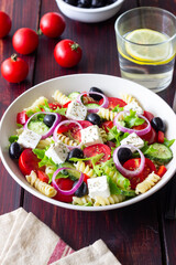 Greek pasta salad with feta cheese, tomatoes, onion, cucumbers, peppers and olives. Healthy eating. Vegetarian food.